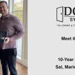 Four coworkers indoors pose with small black boxes; to the right is a gray panel displaying the DOOR SYSTEMS logo, 'Meet the DSI Team Vol. 3', and '10-Year Anniversaries Sal, Mario, Trineice, Phil'